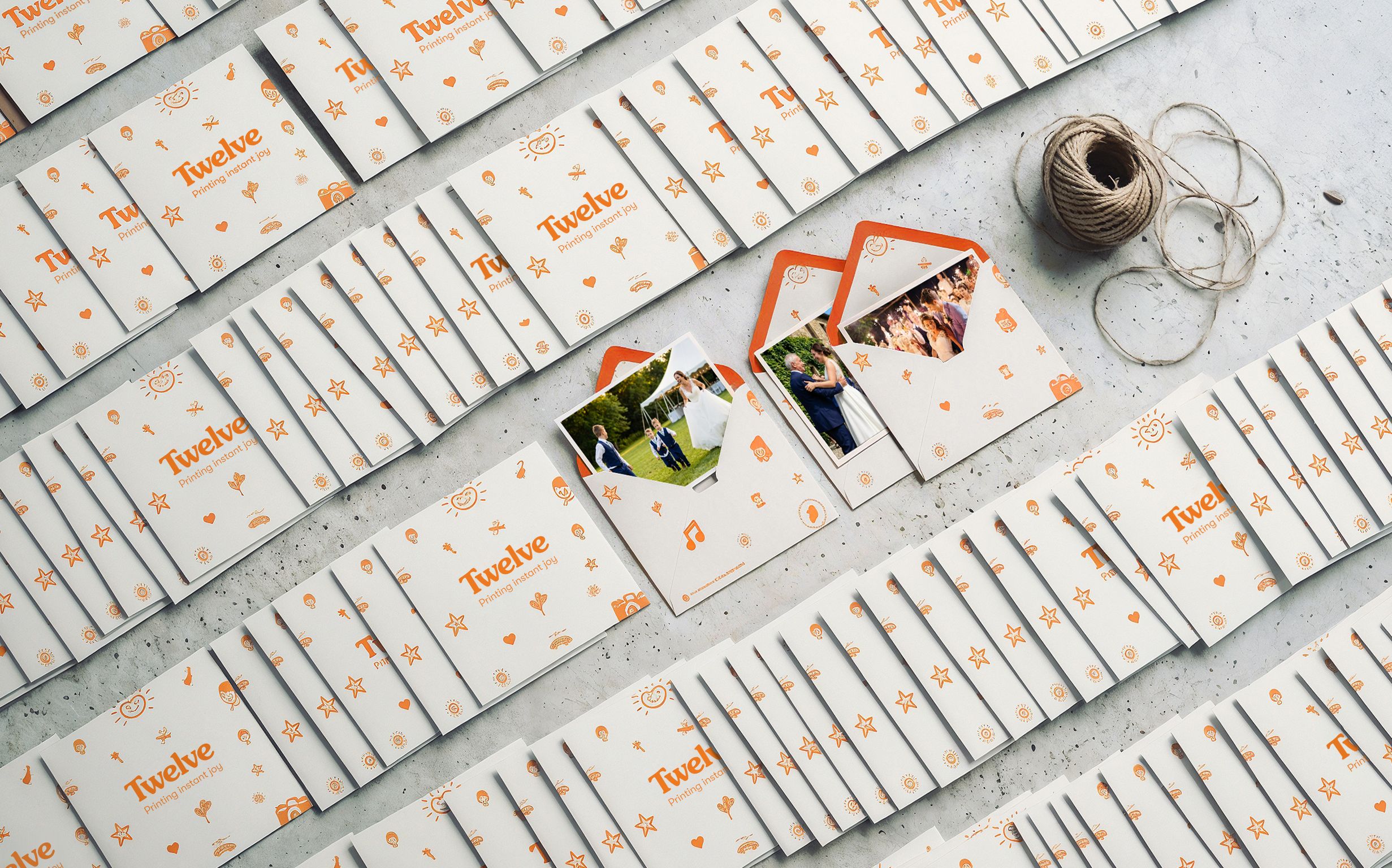 Dozens of unmarked kraft envelopes laid out in neat overlapping rows on pale concrete, shot from above, a few with matte prints slipping out.
