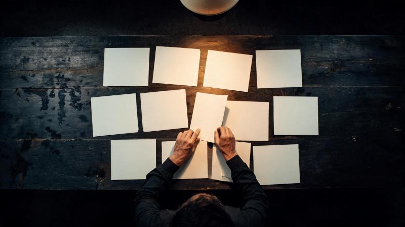An art director's hands choosing one print from a dozen laid out under a single lamp