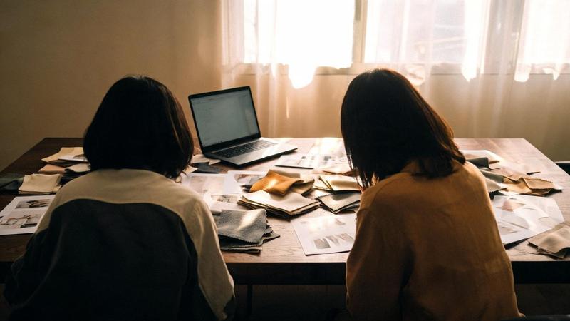 Two colleagues working side by side over swatches and layouts at a large table